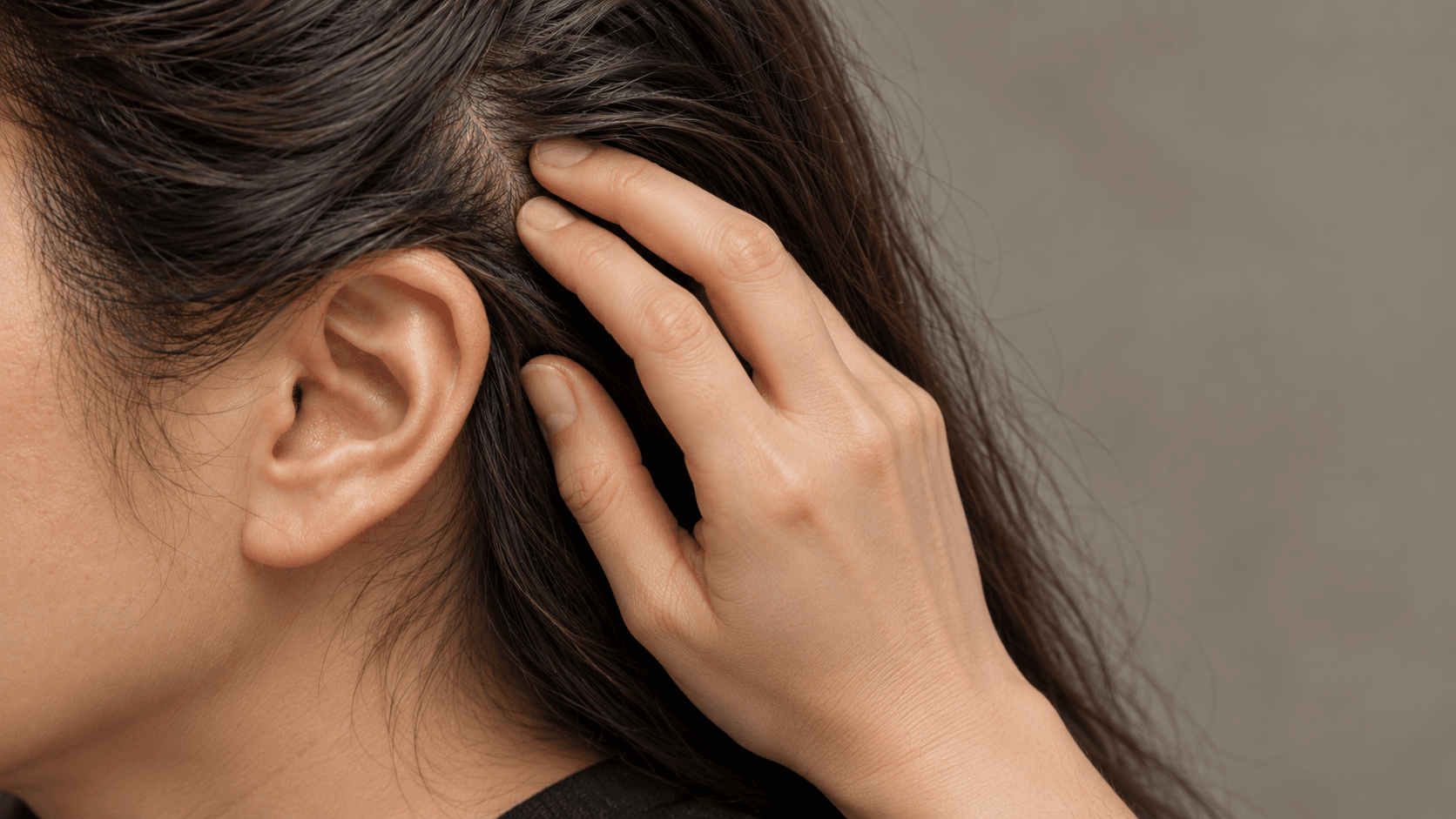 Itchy scalp: woman with dark hair gently pressing her fingertips to the scalp above her ear