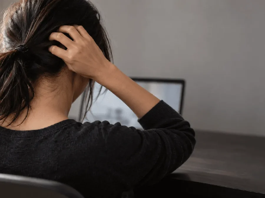 Itchy scalp and stress: woman at a laptop scratching the back of her head