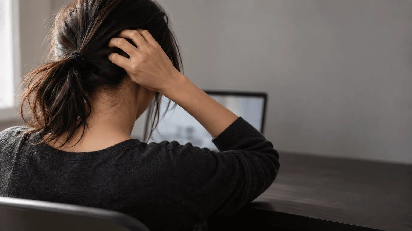 Itchy scalp and stress: woman at a laptop scratching the back of her head