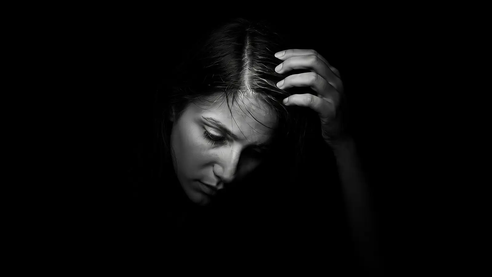 Woman looking down and running her fingers through her hair at the parting